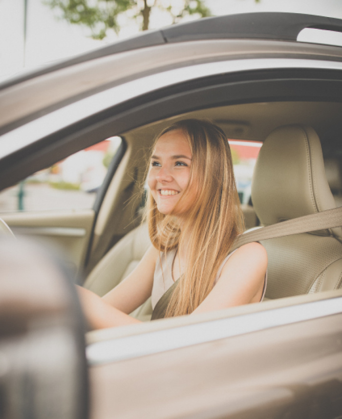 young woman smiling in drivers seat of car