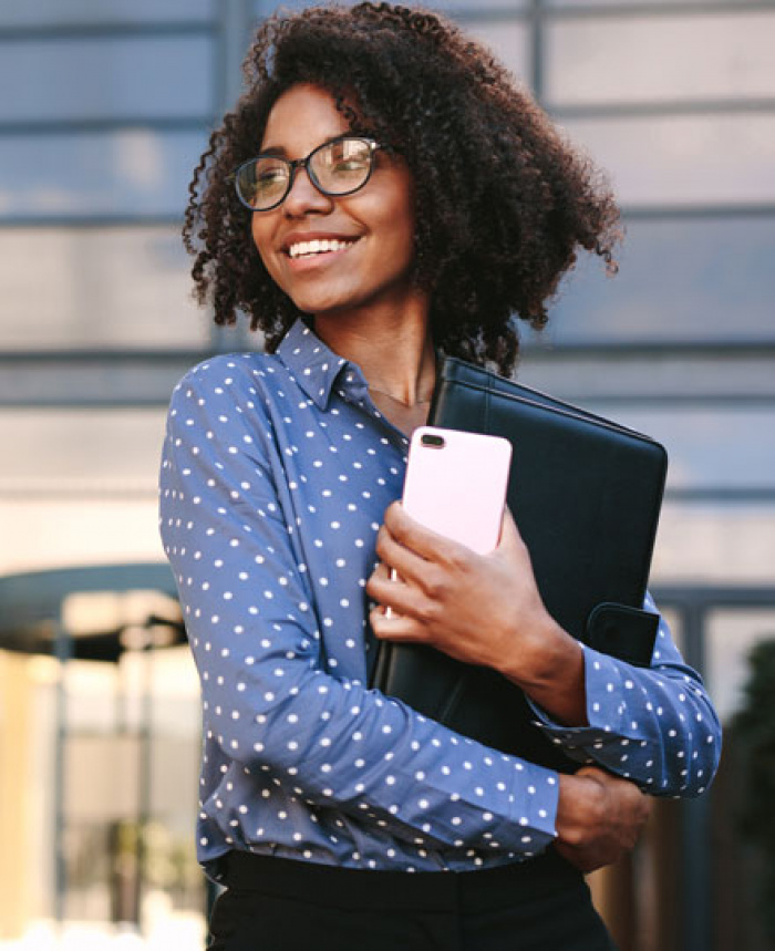 Woman outside office building holding phone and portfolio