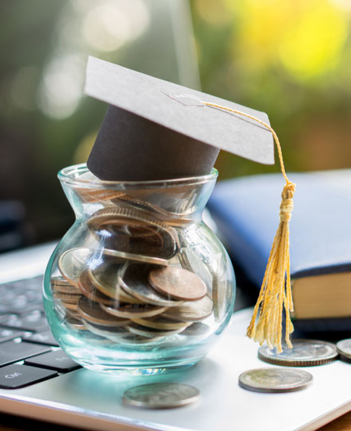 Graduation cap atop of jar of coins atop a laptop