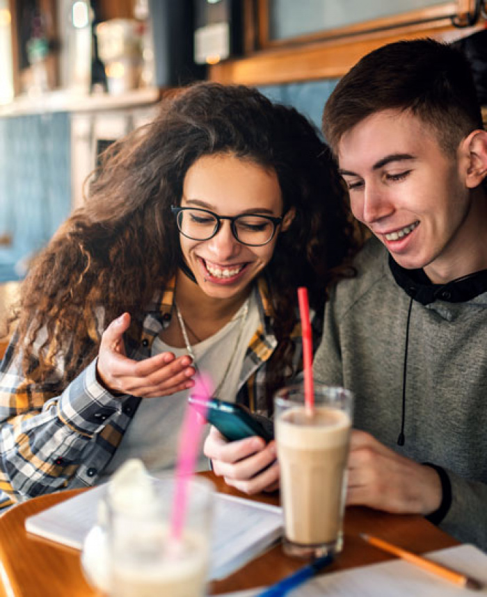 Teens checking their mobile banking while enjoying milkshakes.